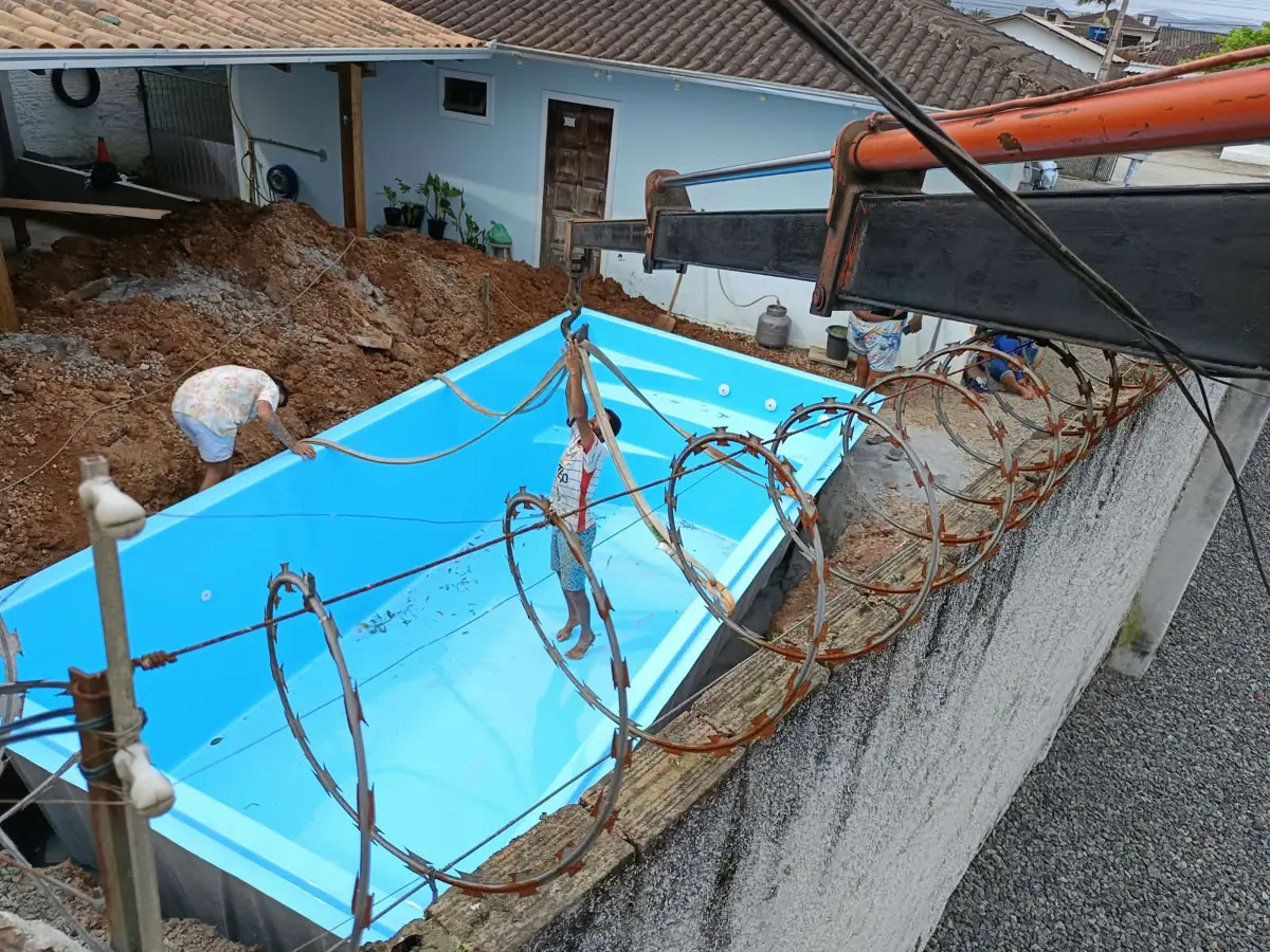 Piscina de fibra azul sendo assentada com munck na escavação do quintal