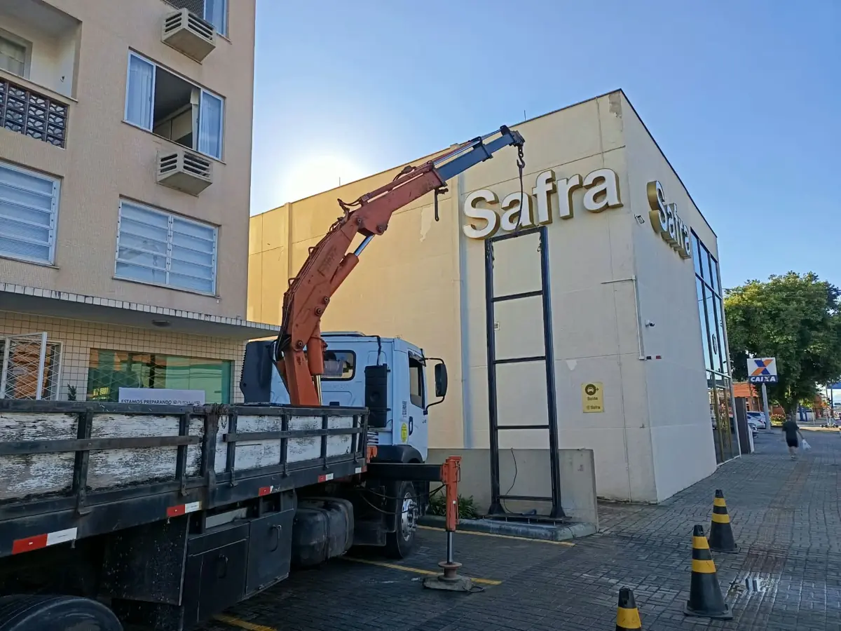 Caminhão munck instalando estrutura de totem na fachada de agência bancária em Joinville