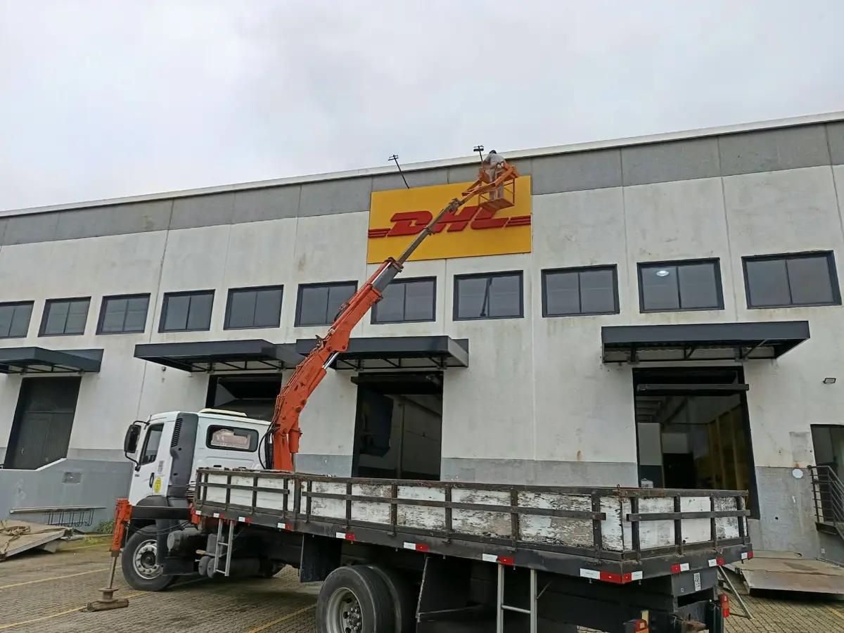 Caminhão munck instalando letreiro na fachada de um galpão logístico em Joinville