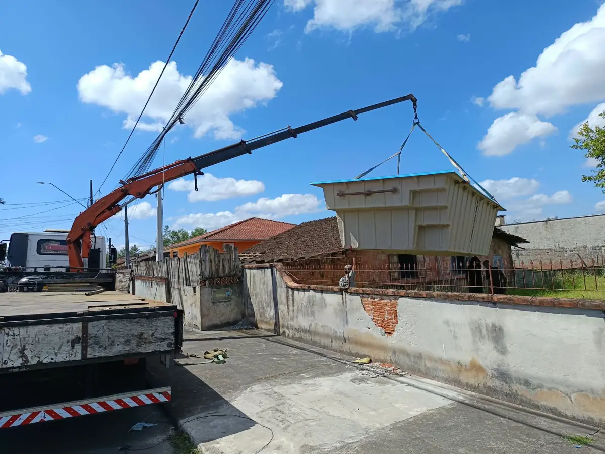 Munck passando piscina de fibra por cima do muro de uma casa em Joinville